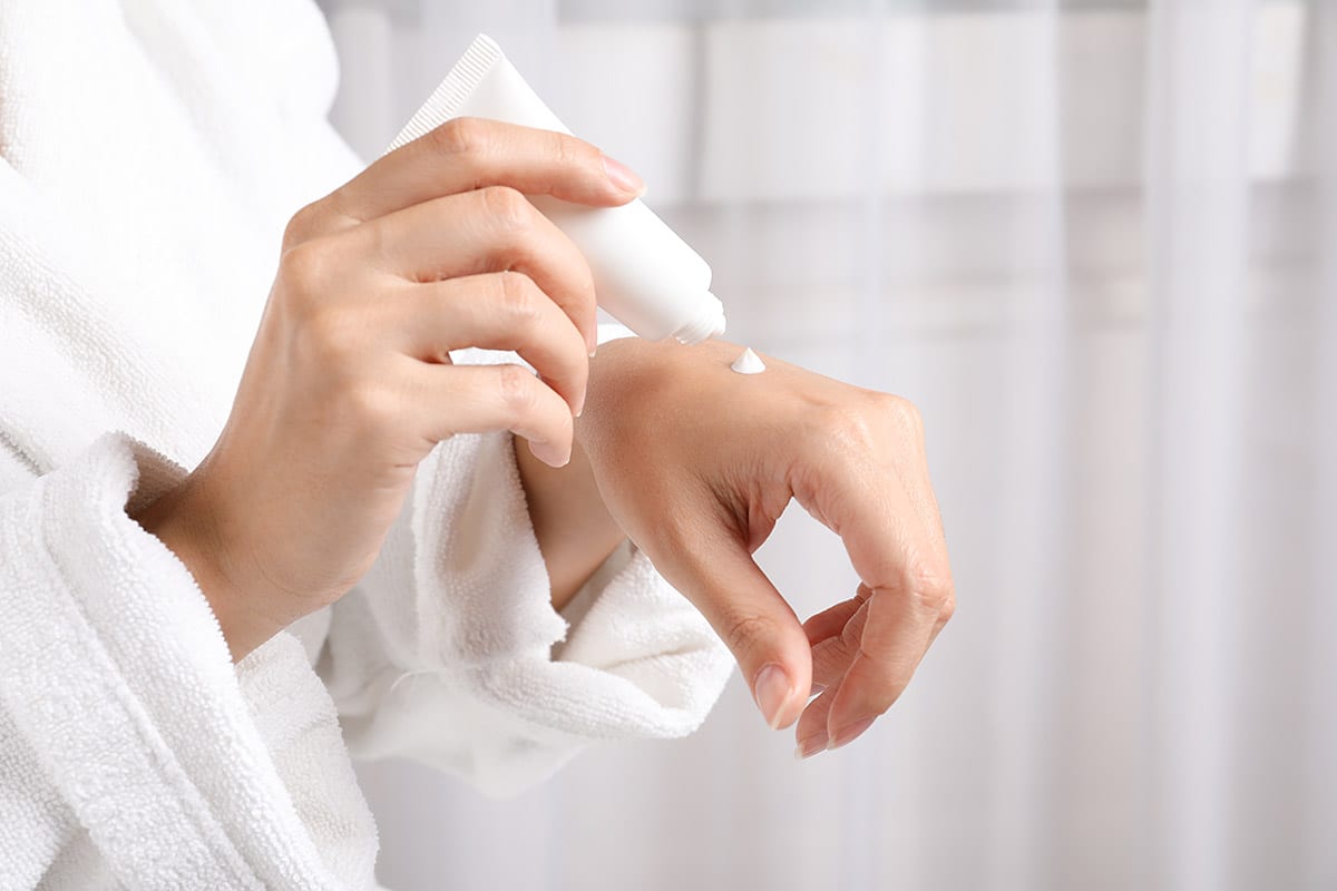 Woman applying moisturizer to hand demonstrating how to Take Care of Combination Skin in the Winter